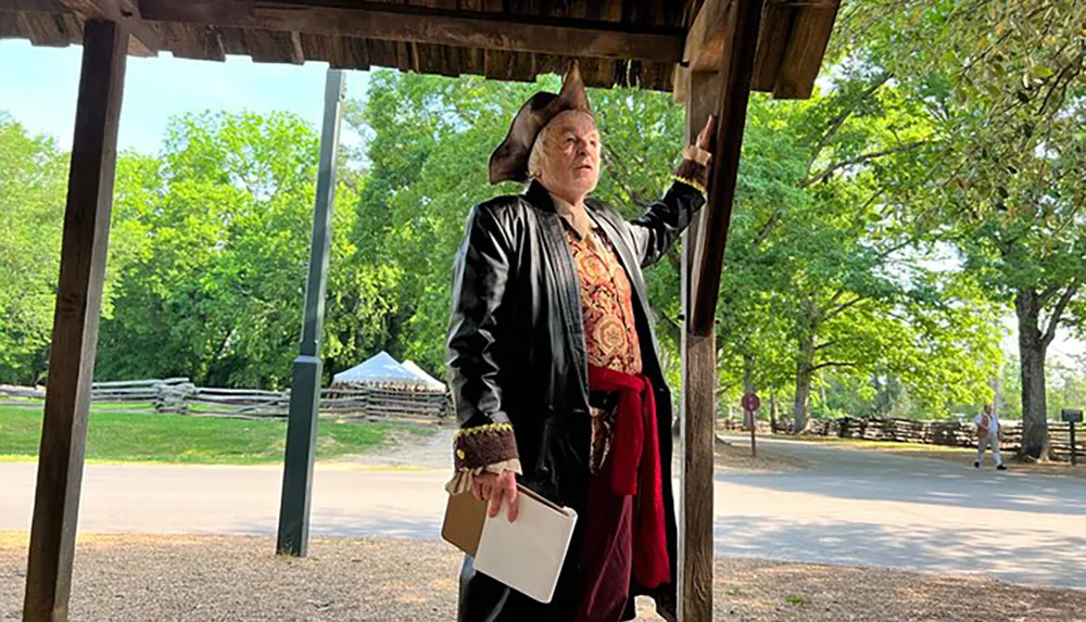 A person is standing under a structure gesturing upwards while wearing historical costume and holding a book seemingly portraying a historical figure or reenactor