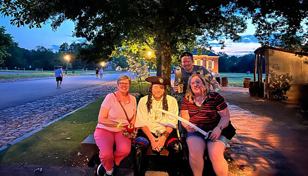 A group of people is smiling for a photo at twilight with one person dressed in pirate attire in a park-like setting
