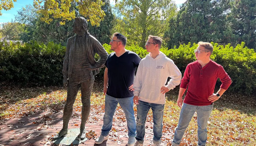 Three men mimic the pose of a statue standing confidently with hands on hips in a sunny outdoor setting