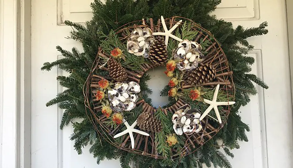 The image shows a decorative wreath adorned with pinecones starfish and green foliage hung on a white door