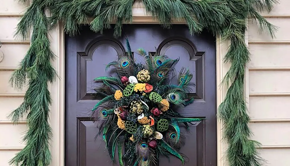 A dark door is adorned with a vibrant peacock feather wreath and framed by lush green garlands on each side