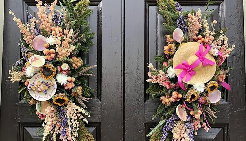 A black door is adorned with two symmetrical floral arrangements featuring a hat plates and seashells creating a whimsical and decorative installation