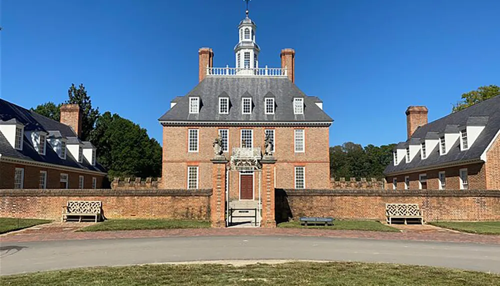 This image shows a large historic brick building with a distinctive cupola on top set against a clear blue sky