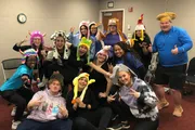 A cheerful group of people are posing for the camera, many wearing fun animal-themed hats, and making playful hand gestures.