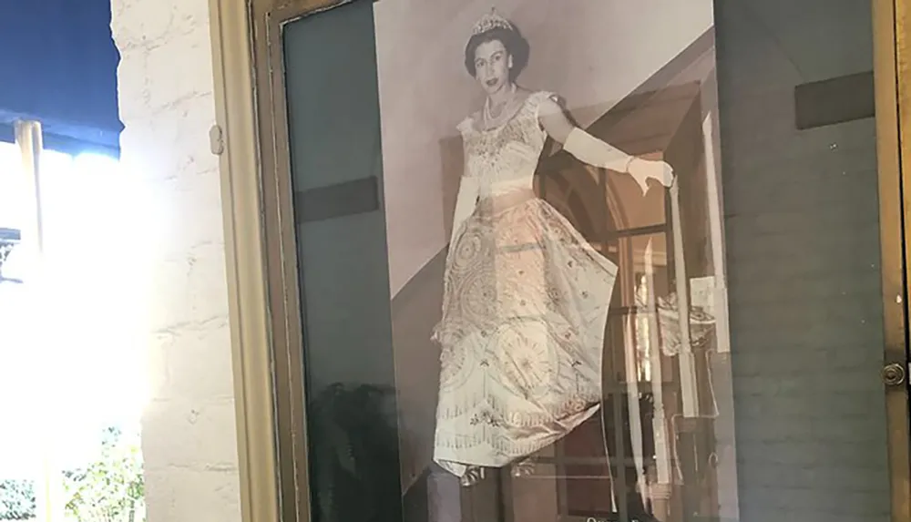 The image shows a life-size photograph or poster of a woman in regal attire displayed behind a glass door creating a slightly reflective surface with visible surroundings