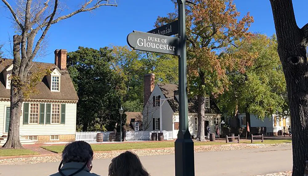 A street sign reading Duke of Gloucester is in the foreground with colonial-style houses and trees with autumn foliage in the background