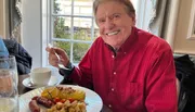 A cheerful person is enjoying a breakfast meal at a table by the window.