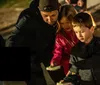 A group of people gather around a lantern at night listening attentively to a person gesturing dramatically likely on a ghost tour