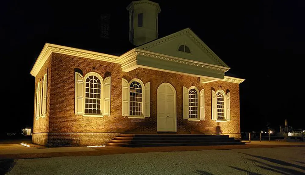 A historic brick building is illuminated by warm lights against the dark night sky