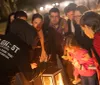 A group of people gather around a lantern at night listening attentively to a person gesturing dramatically likely on a ghost tour