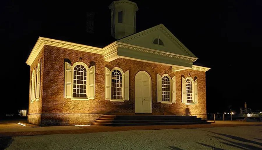 A historic brick building is illuminated at night, highlighting its classical architecture and prominent windows and doorway.