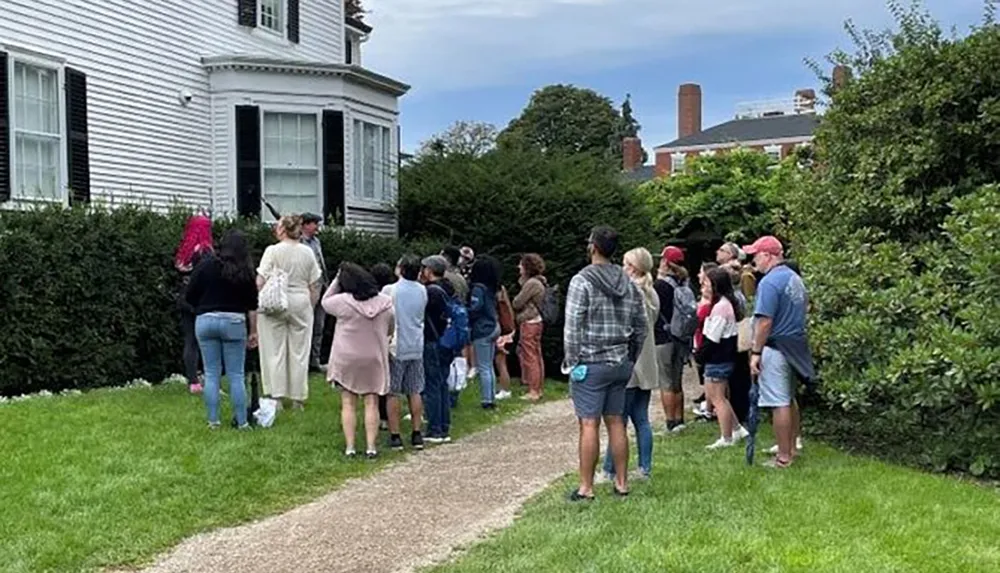 A group of people is queuing outside on a pathway alongside a building possibly indicating an event or an entrance ahead