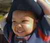 A joyful baby with a wide smile is wearing a large black hat