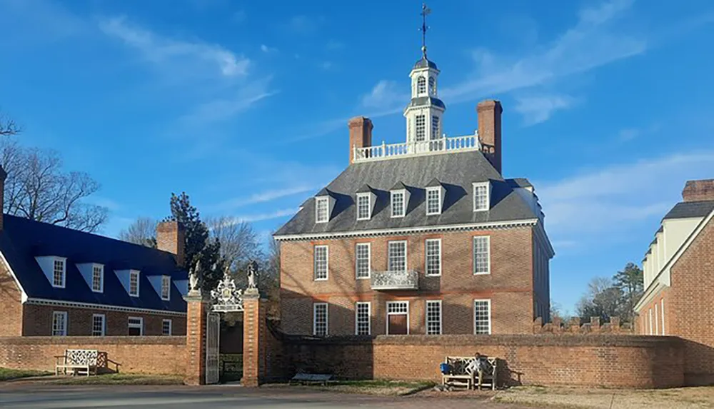 The image depicts the Governors Palace in Colonial Williamsburg Virginia showcasing its grand brick facade and distinctive cupola under a clear blue sky