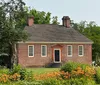 The image shows a traditional brick house with a gabled roof two chimneys and surrounded by lush gardens