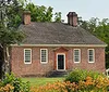 The image shows a traditional brick house with a gabled roof two chimneys and surrounded by lush gardens