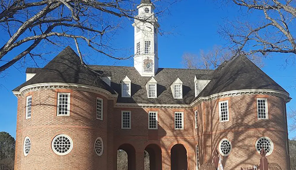 The image shows a large symmetrical brick building with a prominent white clock tower distinctive windows and a clear blue sky in the background