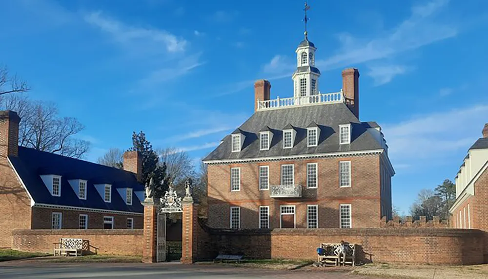 The image shows a historic brick colonial building with a distinctive cupola under a clear blue sky