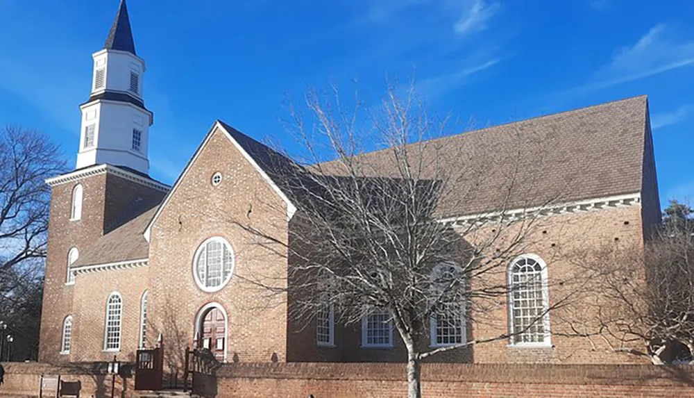 The image shows a traditional brick church with a white steeple under a blue sky