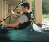 A person is kayaking under a bridge on a calm body of water wearing a life vest and actively paddling
