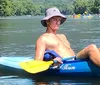 A person is kayaking under a bridge on a calm body of water wearing a life vest and actively paddling