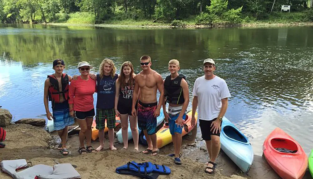 A group of people standing by a river with kayaks smiling for a photo