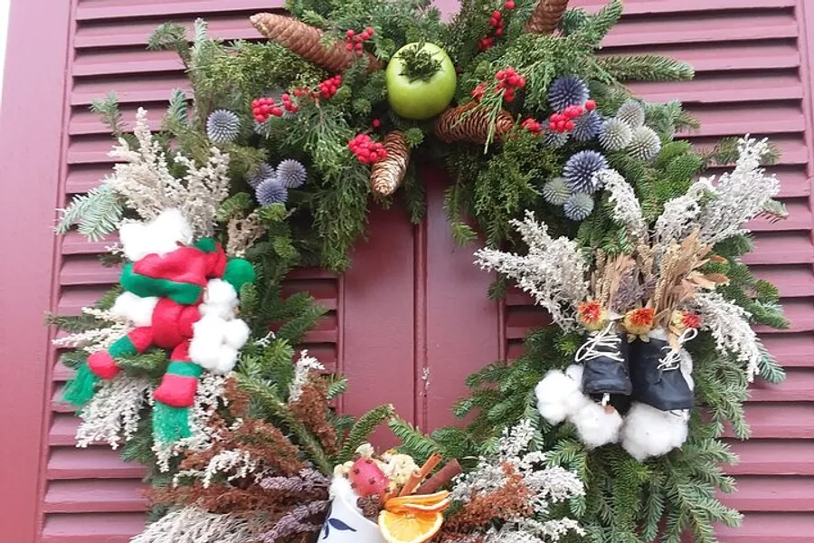 The image shows a festive Christmas wreath adorned with greenery, colorful decorations including red berries and pinecones, and hints of winter themes such as cotton resembling snow, hanging on a reddish-brown door.