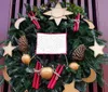 The image shows a festive Christmas wreath adorned with greenery colorful decorations including red berries and pinecones and hints of winter themes such as cotton resembling snow hanging on a reddish-brown door