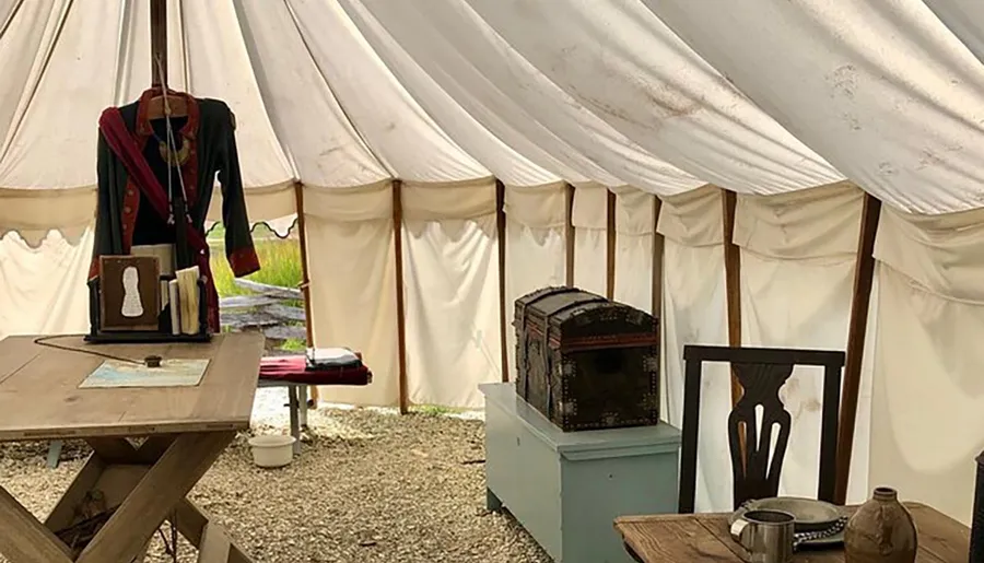 The image shows an old-fashioned military tent with a mannequin wearing a historical uniform, a rustic wooden table, and other period-appropriate items, suggesting a historical reenactment or a living history exhibit.