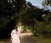 A person in a white outfit is walking down a dimly lit tree-lined path at dusk or night