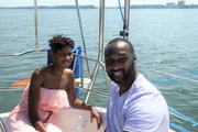 A smiling man and woman are enjoying a sunny day on a sailboat.