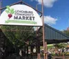 The image shows an entrance sign for the Lynchburg Community Market on a sunny day with people and market stalls visible in the background