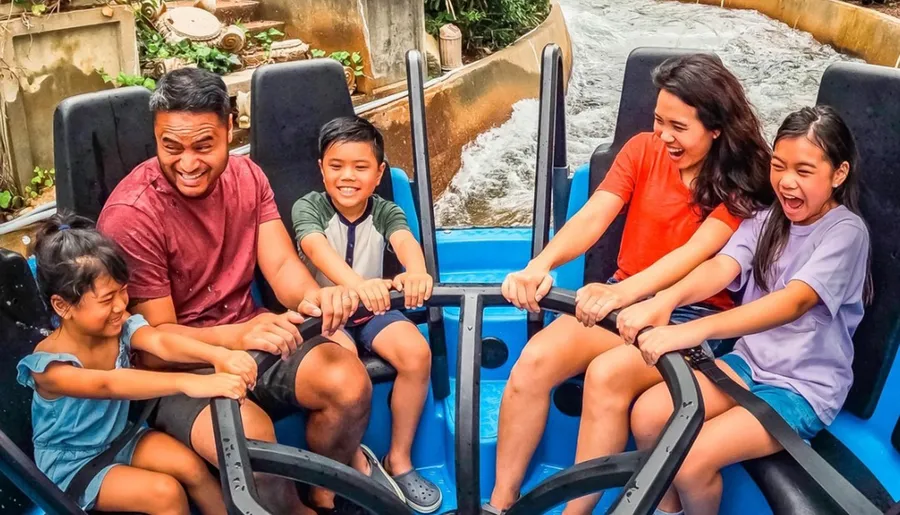 A family of five is joyfully riding a water ride, holding onto the safety bars and laughing.