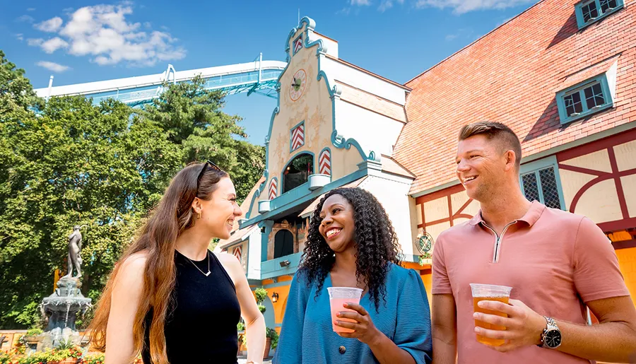 Three people are smiling and enjoying drinks at an outdoor venue with a scenic background.