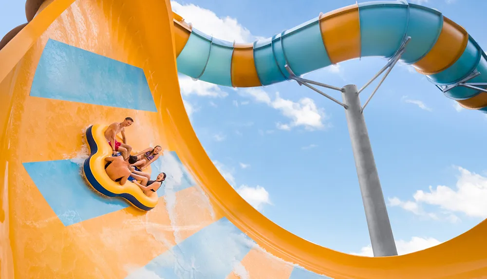 Four individuals are enjoying a thrilling ride down a bright yellow water slide in a blue raft