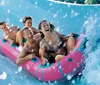 A group of people including children are enjoying a ride on a vibrant colorful water slide in a blue raft surrounded by sprays of water