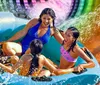 A group of people including children are enjoying a ride on a vibrant colorful water slide in a blue raft surrounded by sprays of water