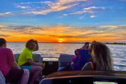 A group of people enjoys a vibrant sunset from the deck of a boat, showcasing a relaxed and picturesque moment.