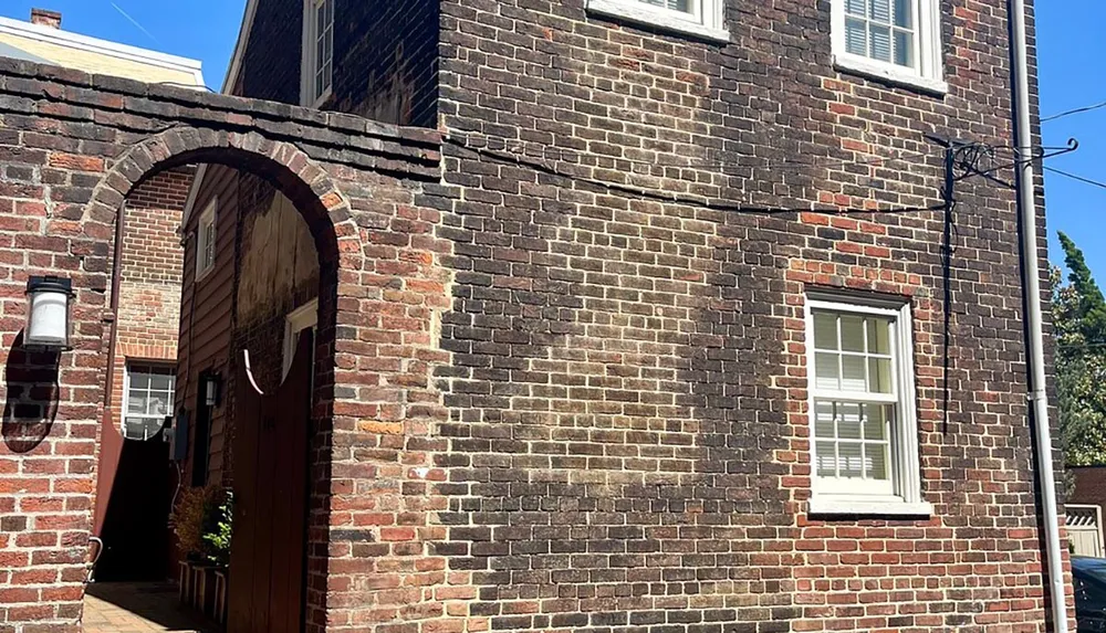 The image depicts a sunny day view of a red brick building with an arched walkway leading to an entrance and a white window to the right