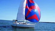 A sailboat with a red and blue spinnaker sails on a clear day with people visible on deck.