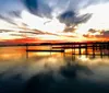 The image displays a serene sunset over a calm body of water with a silhouette of a pier and clouds reflected on the waters surface
