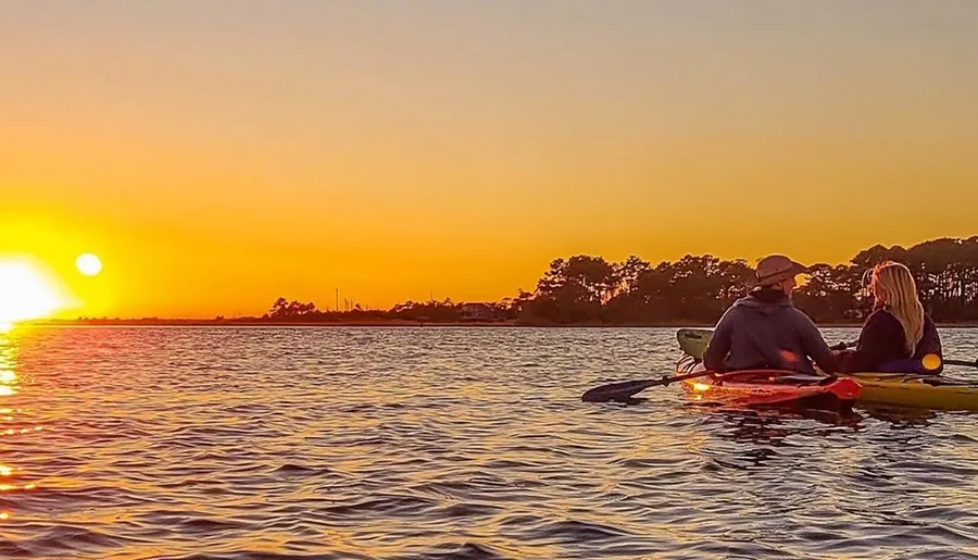 Two individuals are kayaking on calm waters with a beautiful sunset in the background.