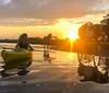 A person in a yellow kayak is paddling near the shore at sunset while a horse and its rider are visible in the background creating a serene silhouette against the glowing sky