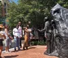 A group of people interacts with and observes a large sculptural installation on a sunny day