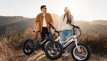 A man and a woman are standing with electric bicycles outdoors, enjoying a sunny day.