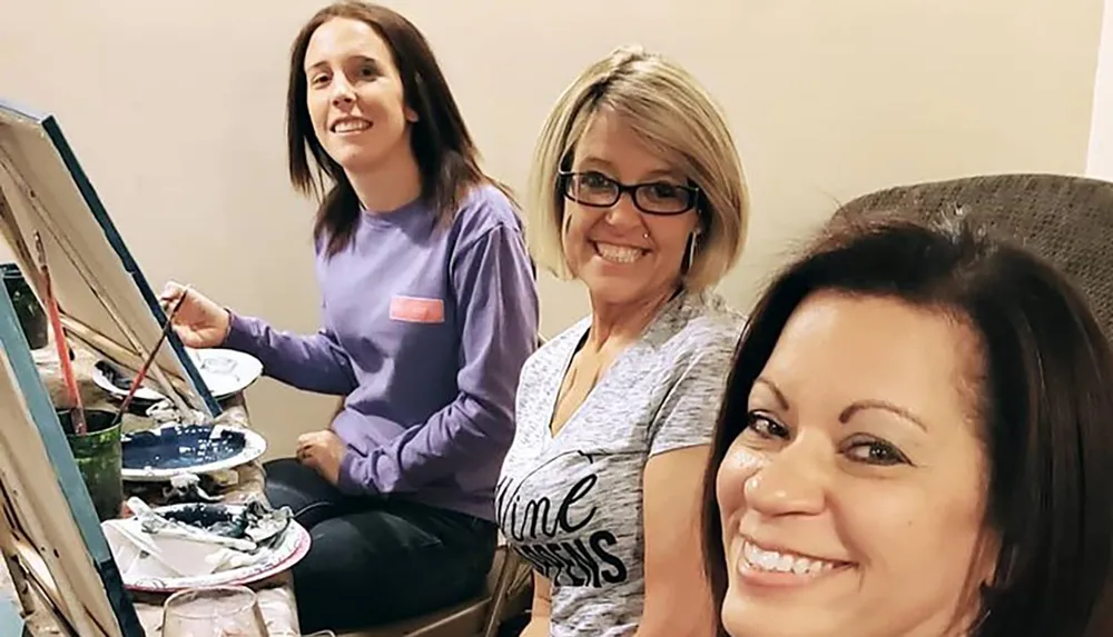 Three women are smiling and enjoying a painting class together
