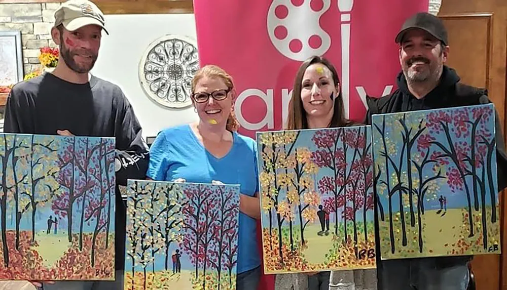Four individuals are standing side by side each proudly holding up a colorful painting of a tree scene