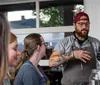 A group of people is engaged in outdoor dining with one person explaining or serving a dish at the table