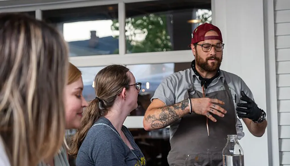 A chef with tattoos is explaining something to an attentive audience possibly during a cooking class or demonstration