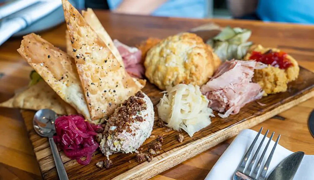 The image shows a charcuterie board with various items including cheese cured meats pickles a spread and flatbread crackers presented on a wooden board